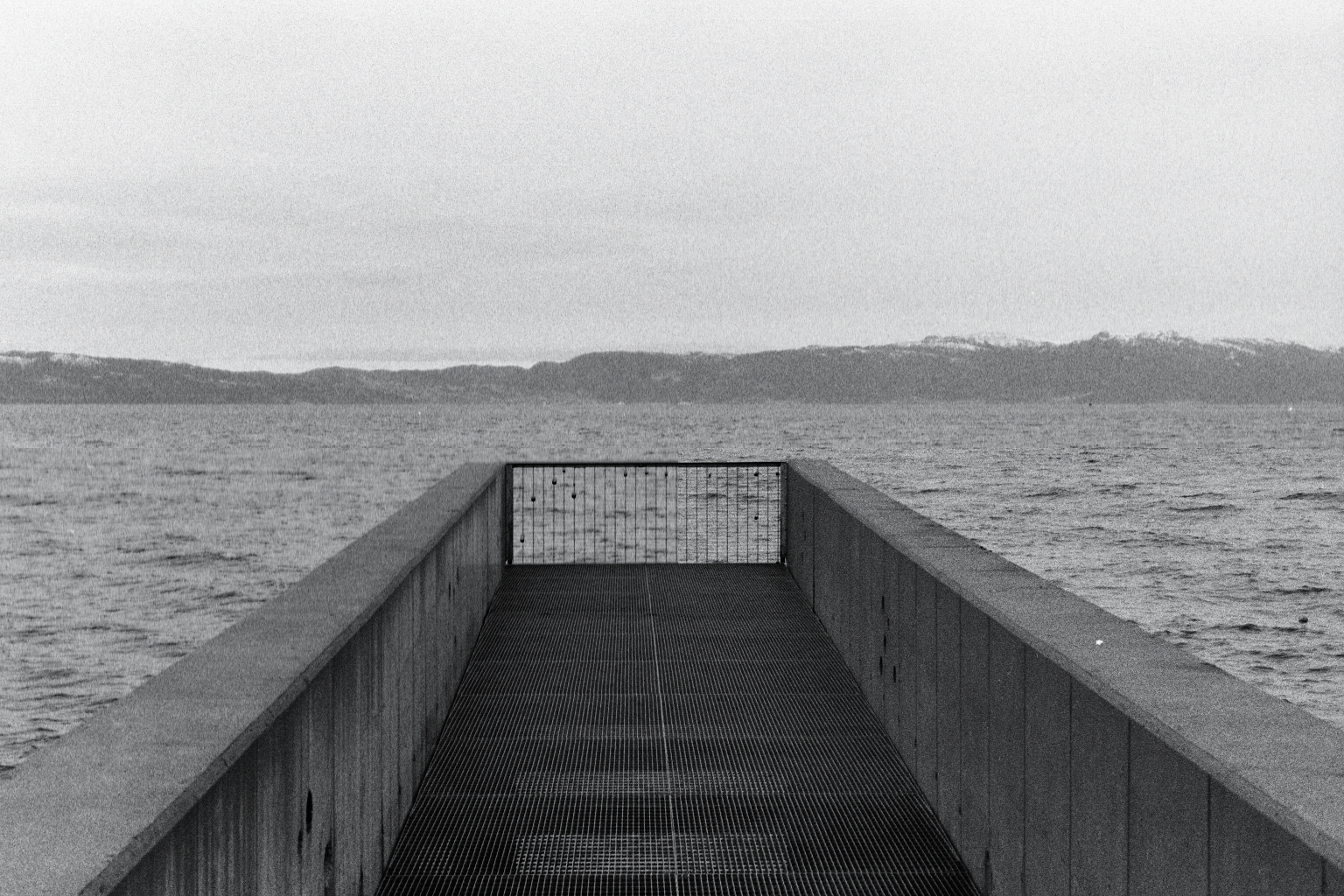 Concrete pier reaching out into the Trondheim fjord under an overcast sky.